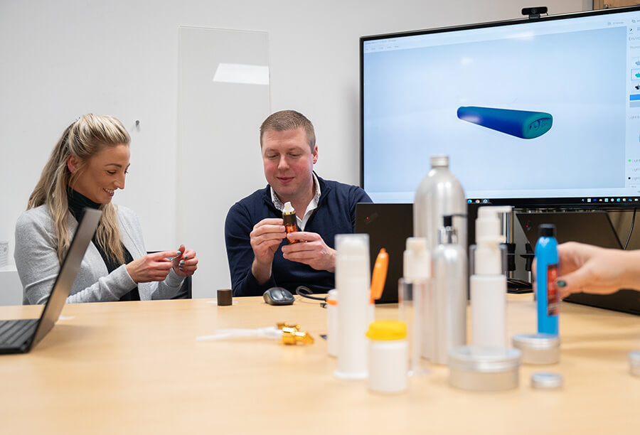 BlueSky team at table, looking at variety of bottles and packaging, with render on TV screen